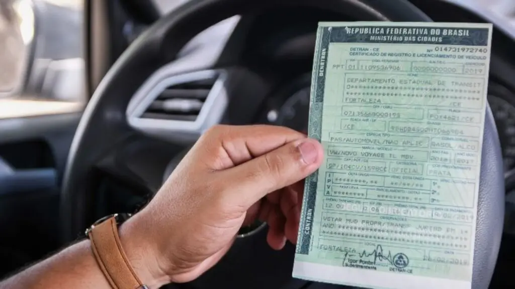 Foto de uma pessoa segurando o seu IPVA dentro do carro