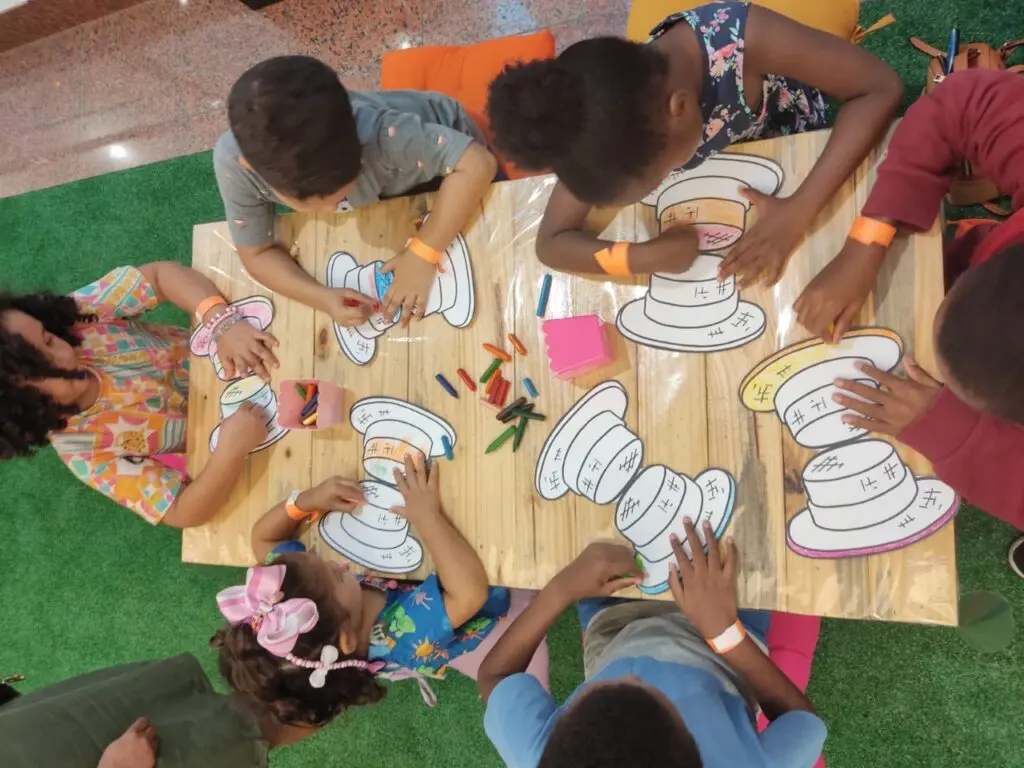 Foto ilustrativa de crianças em volta de uma mesa realizando pinturas em papel, com lápis coloridos