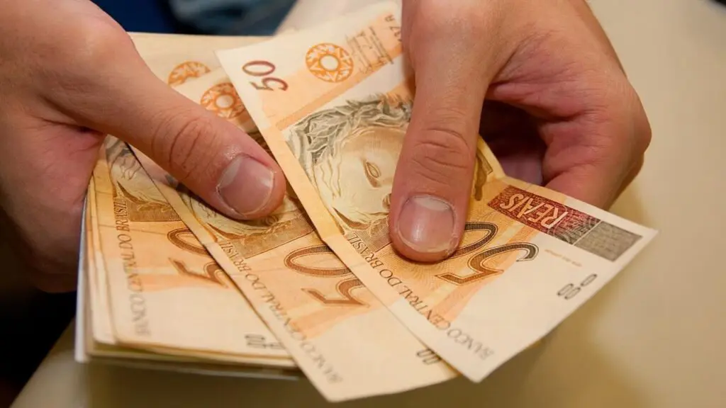 Deputados Estaduais aprovam auxílio financeiro de até 3 mil reais para famílias atingidas pelas fortes chuvas no ES Notas de 50 reais sendo contadas por uma pessoa