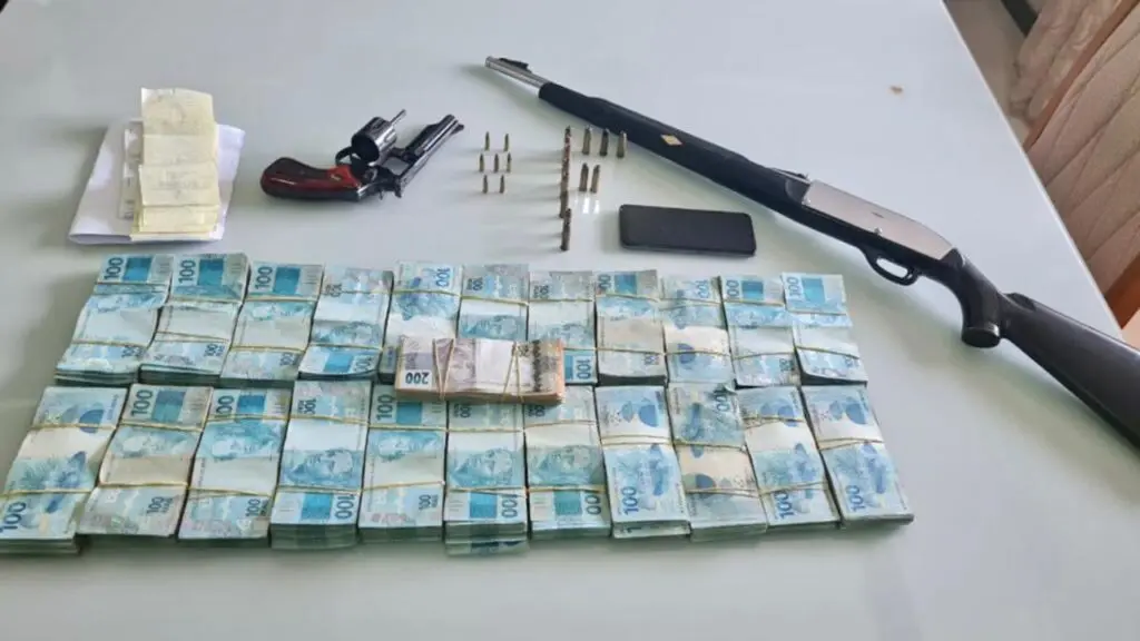 Força Tarefa deflagra megaoperação contra organização criminosa ligada ao tráfico de drogas no ES Sobre uma mesa branca da Polícia bolos de notas de 100 reais e duas armas