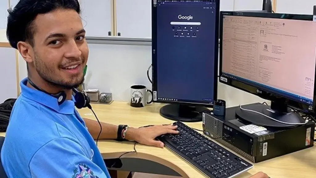 Governo abre mais de 1.300 vagas de estágio em órgãos e secretarias do estado no ES Foto de um estagiário sentado em frente de um computador sorridente