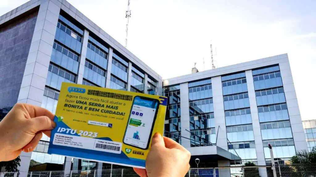 Foto de uma pessoa segurando o boleto do IPTU 2023 em frente à sede da prefeitura da Serra