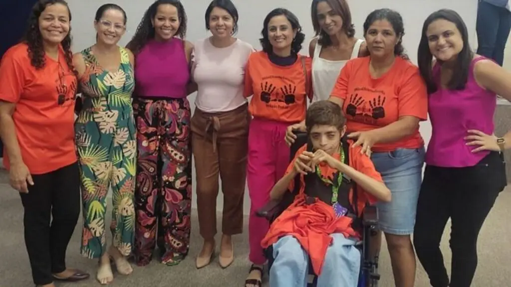Vereadores aprovam projeto da Prefeitura cria cartão de atendimento prioritário para cuidadores de pessoas com deficiência na Serra foto de 8 mulheres abraçadas e no centro da foto um rapaz cadeirante posando para foto da comemoração a aprovação do projeto que criara um cartão com atendimento priorizado e beneficios a cuidadores e pessoas PCD's na Serra