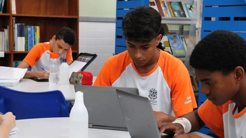 SEDU abre 120 vagas com bolsas de R$ 800 para alunos do Ensino Médio na Grande Vitória Foto em uma sala de aula três alunos estudando em seus notebook's