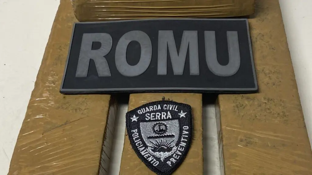 ROMU da Serra arrocha suspeito e apreende 4 tabletes da maconha na Serra Sobre uma mesa branca 4 tabletes de maconha embalados, e sobre os tabletes dois patchs pretos bordados em um escrito ROMU, e no outro Guarda da Serra policiamento preventivo