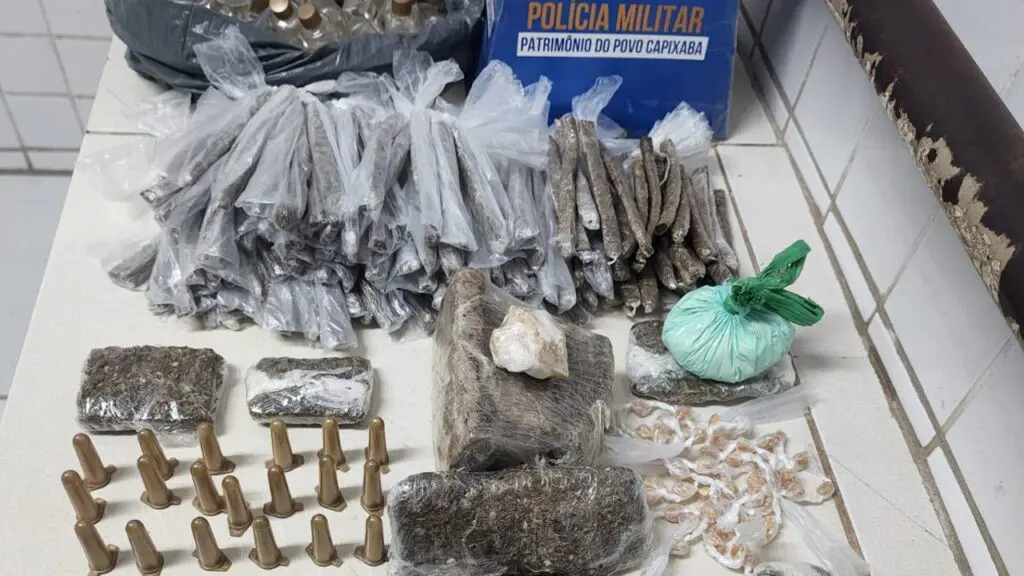 Polícia Militar detona biqueira na Serra com auxílio do P2 e do cão Apollo Sobre uma mesa branca da 3ª Delegacia Regional localizada na Serra, 34 pinos de cocaína, 143 buchas de maconha, uma porção de cocaína, 12 pedaços de maconha, 50 pedras de crack, 56 frascos de loló, um pedaço de crack e 35 bolinhas de haxixe, e um material feito de papelão com o símbolo da Policia Militar