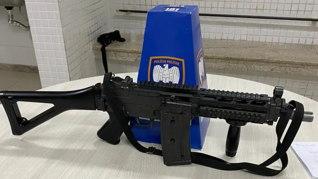 Jovem é morto após tentar assaltar um PM com metralhadora falsa em Cariacica Sobre uma mesa branca um simulacro idêntico a uma metralhadora, e uma propaganda da Policia Militar feita de papelão