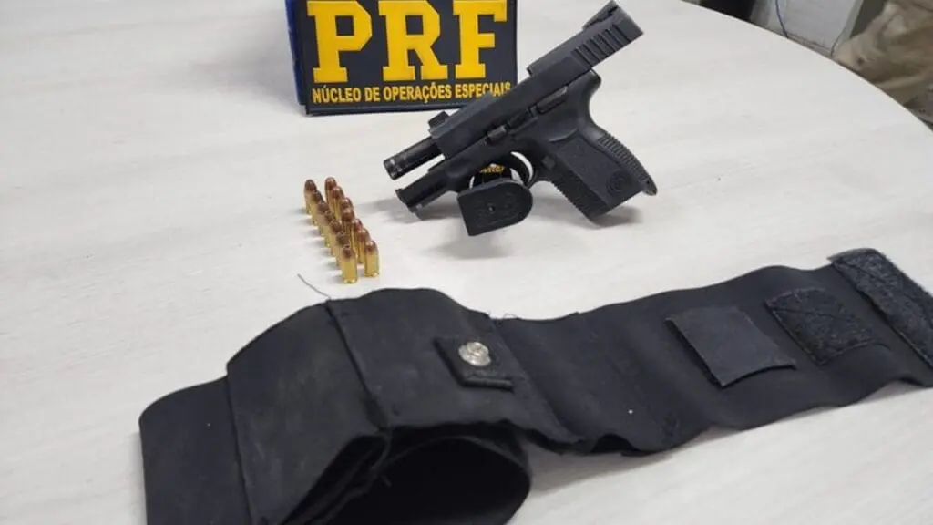 Deficiente acaba detido pela Polícia Rodoviária Federal após comprar pistola na feira de Aribiri sobre uma mesa branca uma psitola tauros 14 munições da pistolas enfileiradas e um coldre