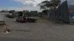 Foto de terreno com piso de paralelepípedo próximo ao bairro José de Anchieta na BR-110 na cidade da Serra, no local há duas camionetes estacionadas e pessoas paradas em volta.