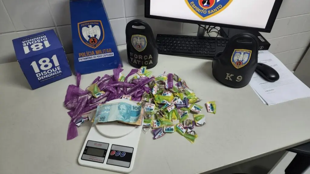 Polícia Militar flagra vapor vacilando durante plantão e detona biqueira em Planalto Serrano Sobre uma mesa branca um monitor um teclado braçadeiras da Polícia Militar, uma da equipe K9 e outra da Força Tática além do material apreendido 533 reais em espécie, 20 buchas de maconha, 47 pedras de crack, 55 pinos de cocaína, drogas com logomarca e uma balança de precisão.