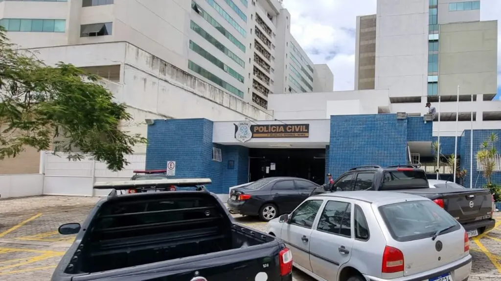 Foto da entrada da 3ª Delegacia situada na Serra, com vários veículos estacionados no patio.