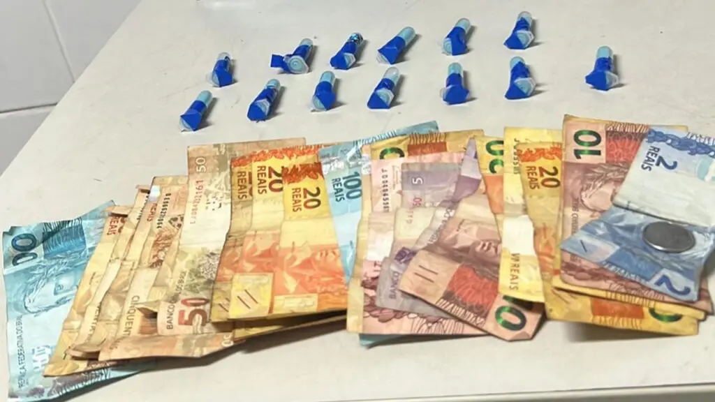 Polícia Militar flagra mulher vendendo droga para cliente próximo de distribuidora em Serra Dourada Sobre uma mesa branca R$ 802,25 em dinheiro, 13 pinos de cocaína