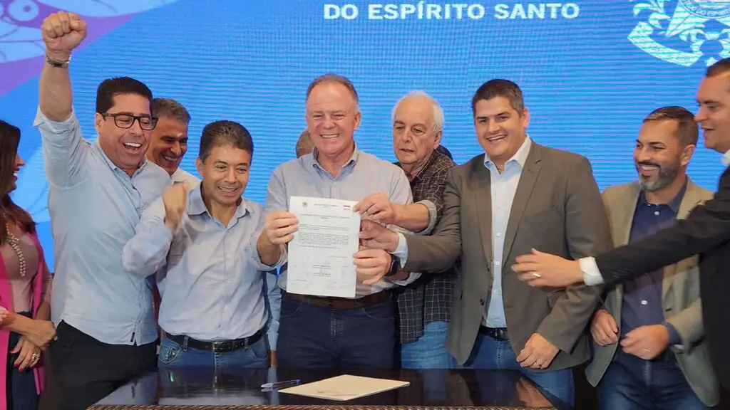 Renato Casagranda anuncia 1,6 bilhão em obras rodoviárias e de infraestrutura no ES Foto Governador Renato Casagrande anunciando investimentos no ES, segurando o documento com 8 politicos ao seu lado