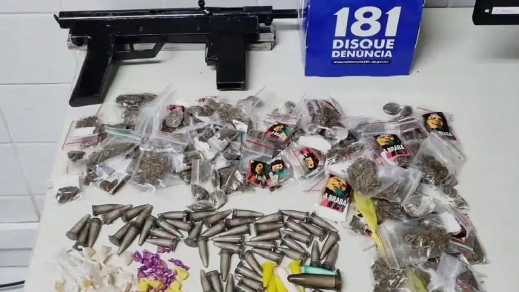 Polícia Militar encontra terreno forrado de drogas após denúncias anônimas na Serra Sobre uma mesa branca uma metralhadora semi-industrial e grande variedade e quantidade de drogas