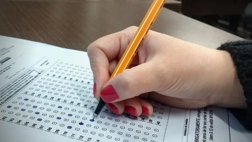 Concurso do CORE abre 98 vagas de nível médio e superior com salários de até R$ 5,5 mil Foto de uma mão feminina preenchendo um gabarito de possível concurso público