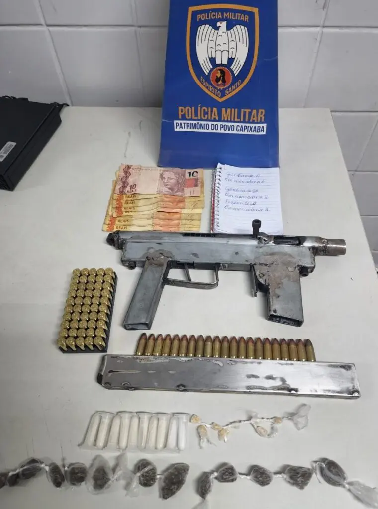 Sobre uma mesa branca uma metralhadora calibre 9mm, 71 munições do mesmo calibre, aproximadamente R$ 170 em espécie, além de pinos de cocaína, pedras de crack e buchas de maconha