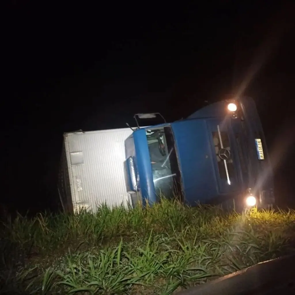 caminhão capotado em um barrando com os faróis acessos