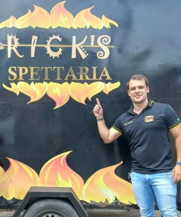 Proprietário ao lado do trailer apontando para o nome do seu negócio Rick's Spettaria, que foi levado pelos Ladrões.
