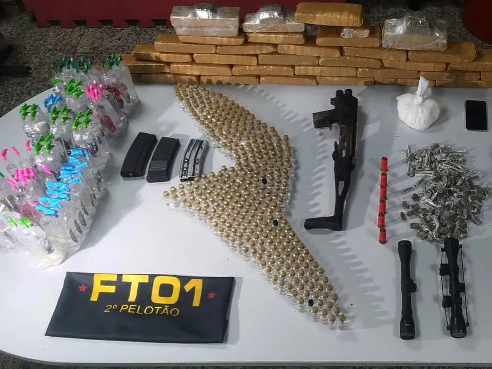 Apreensões da Polícia Militar sobre uma mesa branca, 426 frascos de Lança perfume, 152 buchas de maconha, três carregadores de fuzis, 35 Tabletes de maconha, 500gr de Cocaína, 6 munições calibre 12, duas Lunetas (miras telescópicas para armas), três Capas de coletes com capas balísticas, além de um kit Roni, um adaptador que transforma uma pistola em uma submetralhadora.