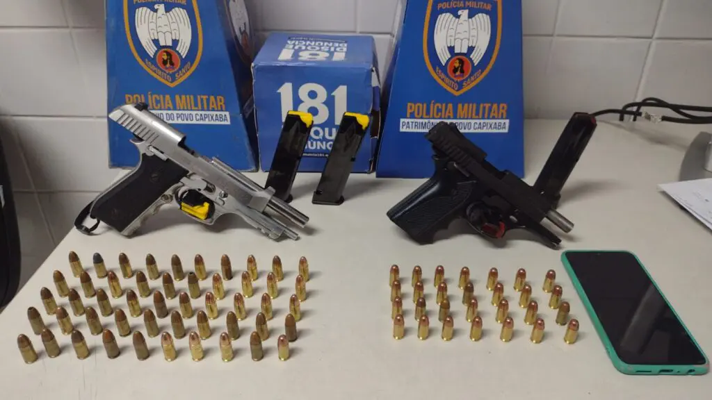 Materiais apreendidos pela Polícia Militar durante a ocorrência, sobre uma mesa duas pistolas, 88 munições além de 3 pentes.