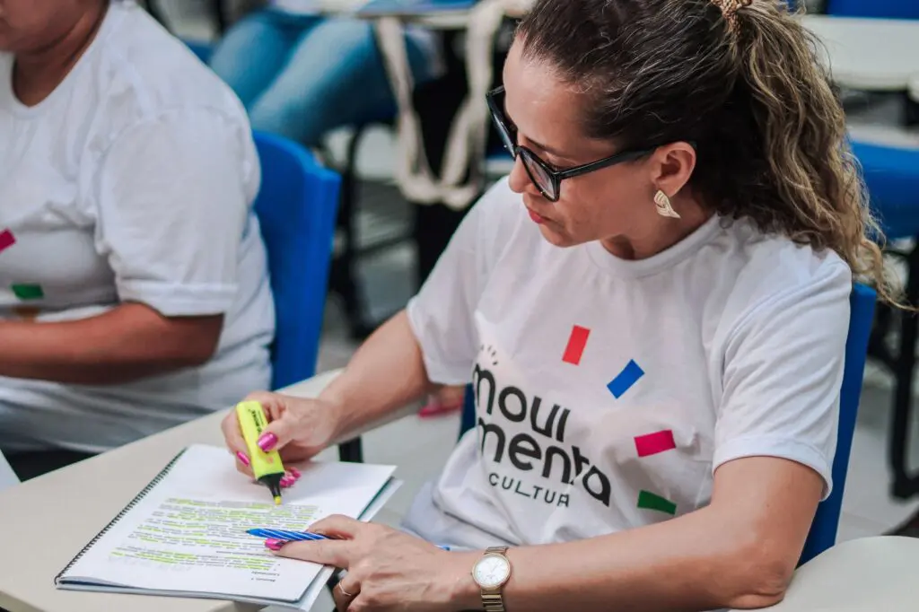 Uma das alunas da oficina - O Avesso da Cena - Empreendedorismo Cultural marcando trechos de uma apostila com caneta marca texto.