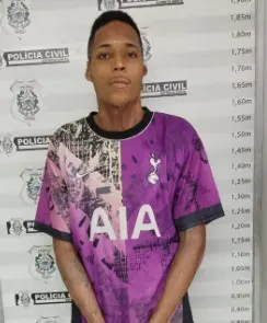 A foto do assaltante na delegacia sendo fichado, Anderson Gouveia da Silva Soares ao fundo o banner da Polícia Civil com a marcação da altura do sujeito.