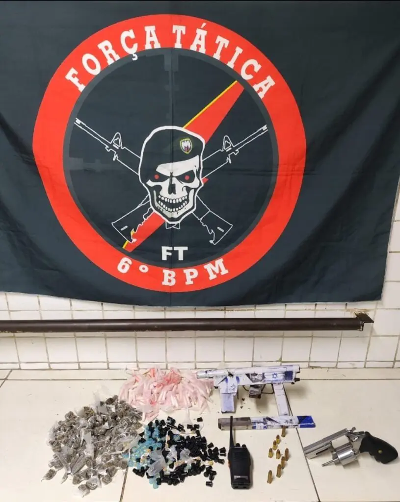 Materiais apreendidos pelas equipes da Força Tática, uma bandeira com o logo da Força Tática do 6º Batalhão, sobre uma bancada um revólver calibre .38, 5 munições calibre .38, 233 buchas de maconha, 130 pinos de cocaína, 211 pedras de crack, além de uma metralhadora "craftada pelos cria" com um carregador sobressalente e 4 munições calibre 9mm. 