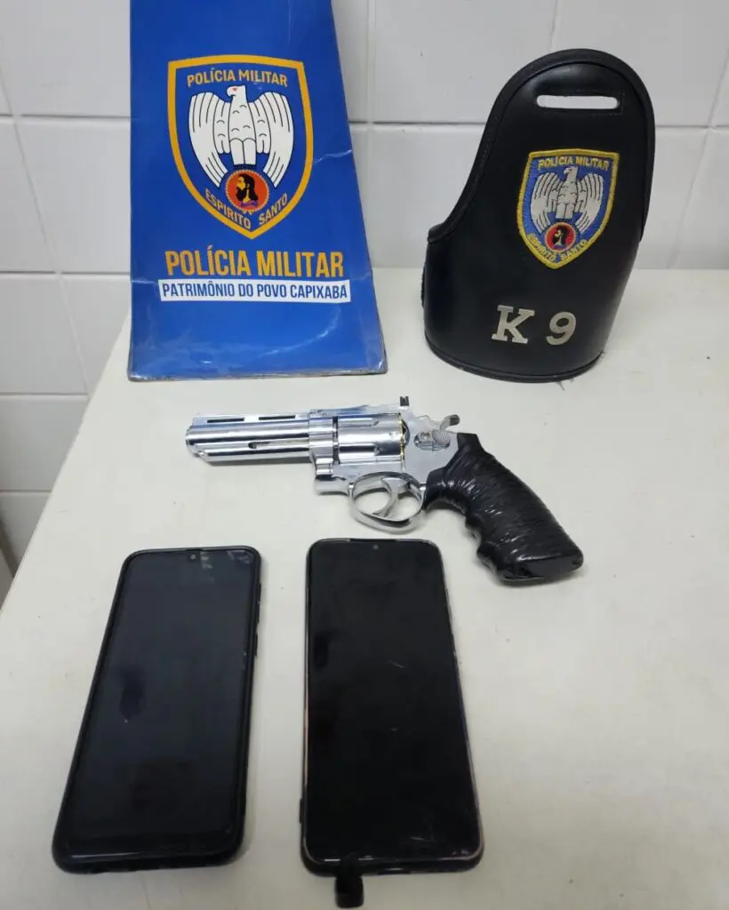 Sobre uma mesa os materiais apreendidos pela equipe da Força Tática, uma réplica de revolver e dois celulares.