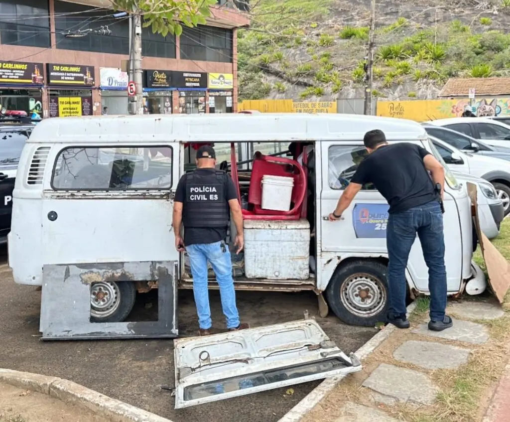 Dois policiais civis realizando buscas em um veículo modelo Kombi, onde um sujeito acusado de latrocínio morava.