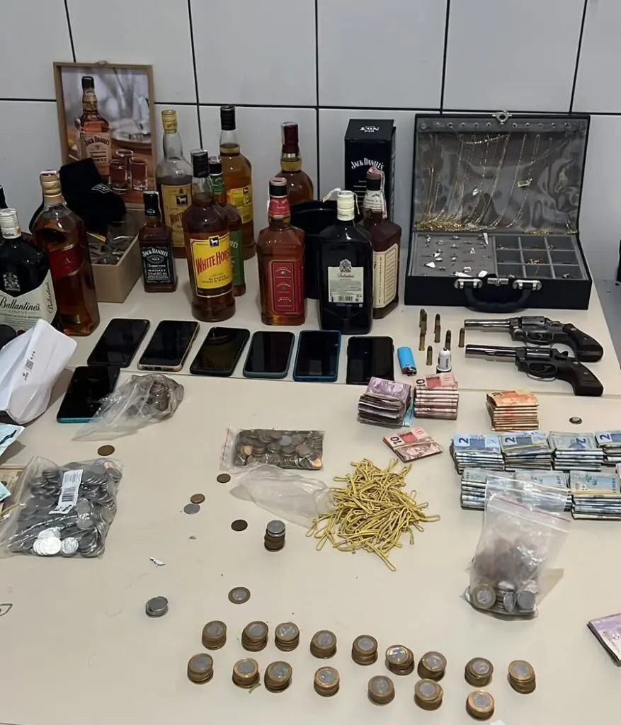 Sobre uma mesa: uma faca, dois revólveres calibre 38, dez munições, R$ 4.253,00 em espécie, $25 dólares, 53 joias, uma placa de ouro de sete gramas, sete celulares, uma touca balaclava, um boné e 14 garrafas de whisky.