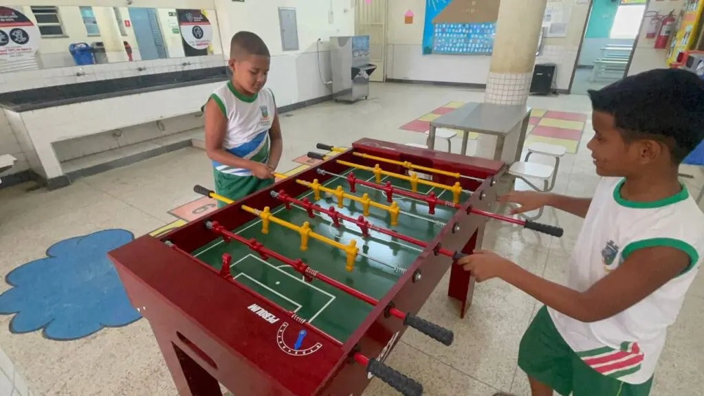 Duas crianças jogando pebolim em um patio de uma escola. 