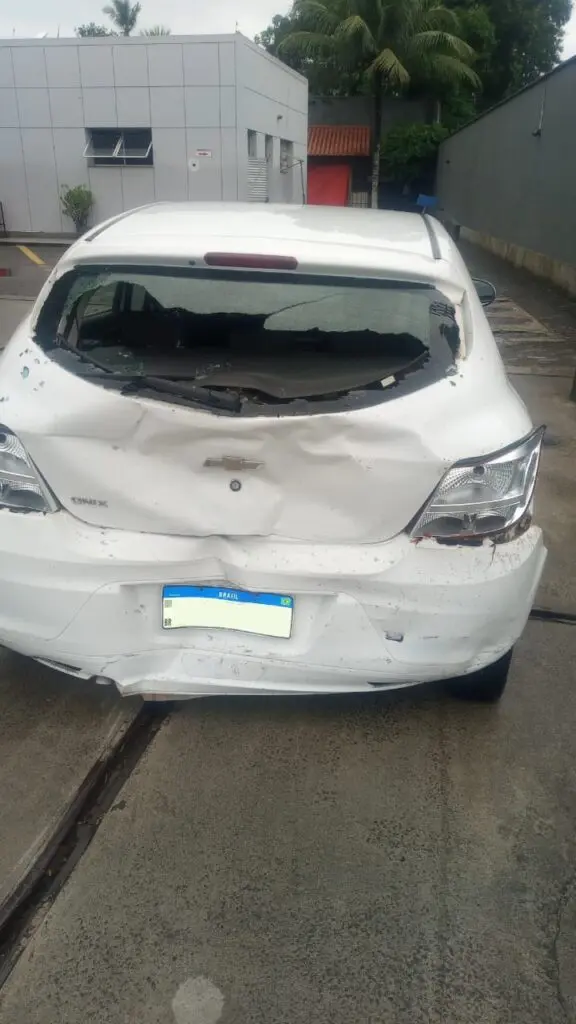 Veículo da vítima após o acidente, com a parte traseira totalmente amassada, estacionado em um posto de combustíveis.