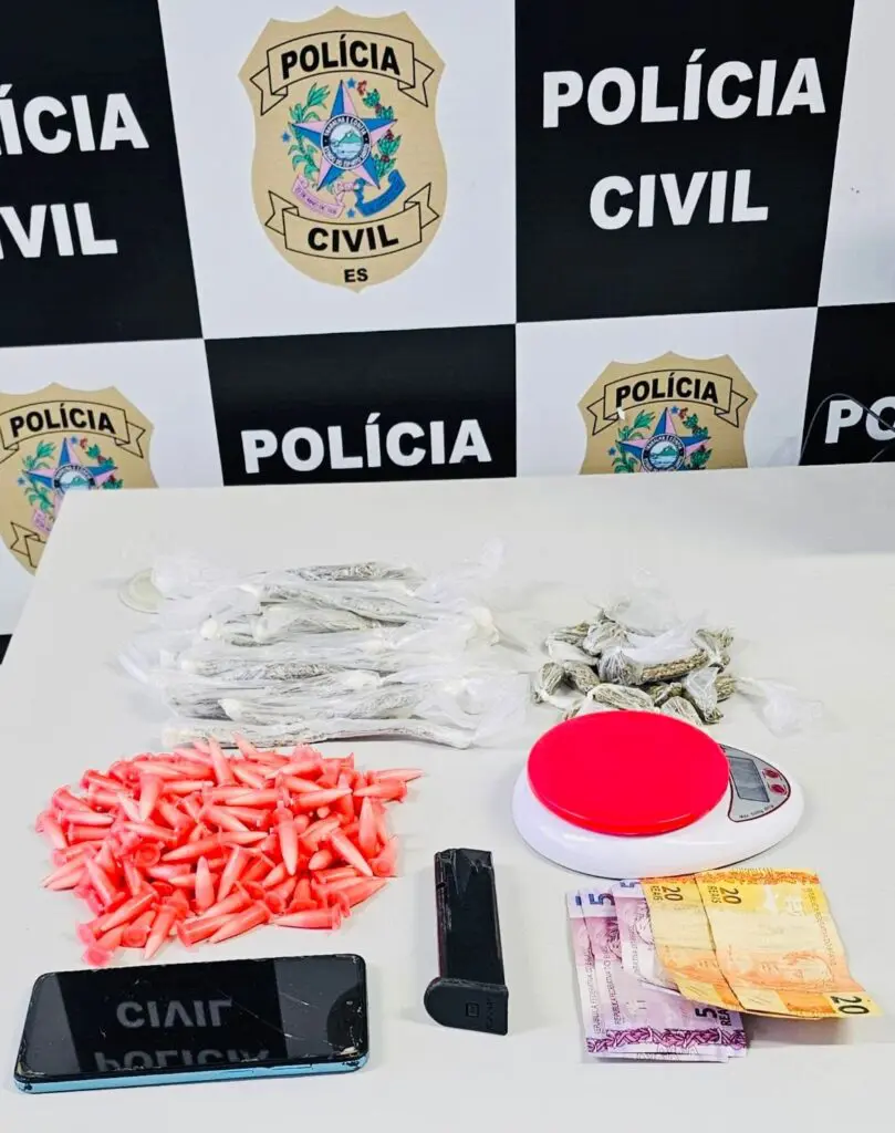 Material aprendido sobre uma mesa uma balança de precisão, um carregador de arma, pinos de cocaína, celular e cedulas de dinheiro.