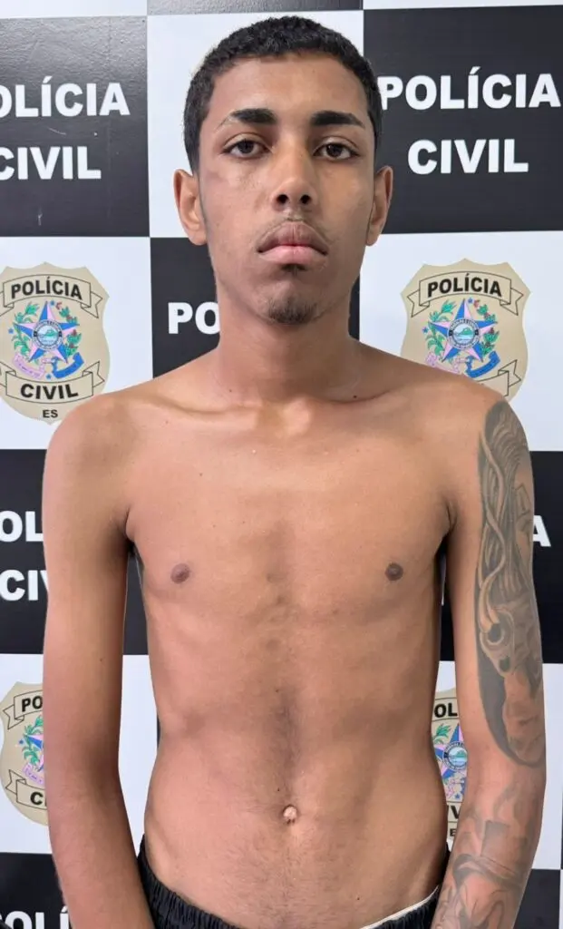 Imagem de um homem (Igor Gabriel da Silva, de 19 anos), parado em frente a uma parede com informações de divulgação da Polícia Civil/DHPP