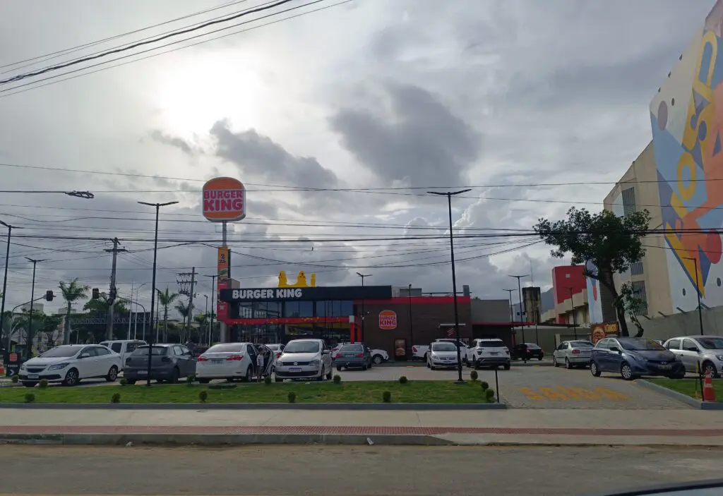 Imagem de uma lanchonete Burguer King com diversos carros estacionados em seu estacionamento. 