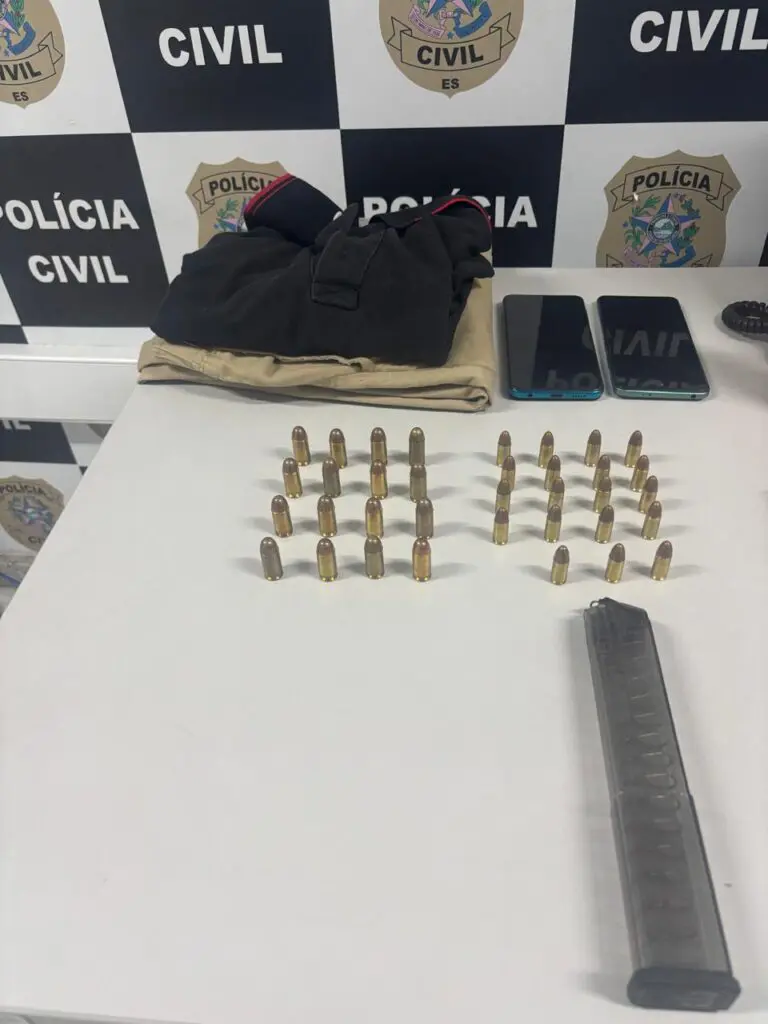 Imagem de materiais apreendidos sobre uma mesa: 19 munições de calibre 9 mm, 16 munições de calibre .45, um carregador alongado de calibre 9 mm, uma camiseta e uma calça e dois celulares.
