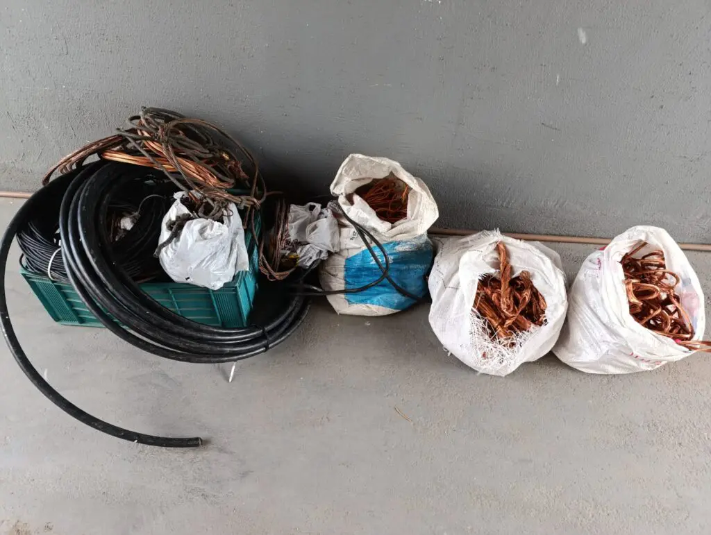 Materiais apreendidos durante a operação da Polícia Civil, sobre o chão pedaços de cabos de cobre, dentro de sacos e caixas.