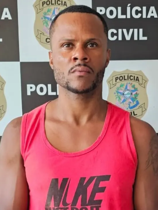 Um homem (Alex Barbosa da Silva, vulgo "Nação"), acusado de homicídio, em frente a um banner de divulgação da Polícia Civil.