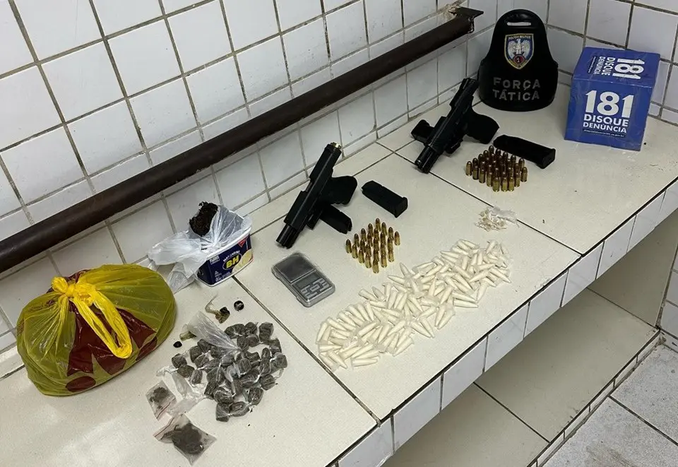 Sobre uma bancada duas pistolas calibres 9mm e .45, carregadores, 29 munições calibre .45, 23 munições calibre 9mm, 105 pinos de cocaína, 42 buchas de maconha, uma sacola com aproximadamente 570g de maconha, 14 pedras de crack, cinco unidades de haxixe e um seletor de rajada.