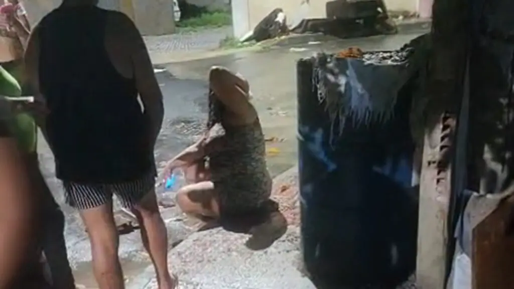 Marido e mulher acabam esfaqueados durante briga familiar na Serra Mulher sentada na calçada, com a mão na cabeça por conta do ferimento, enquanto vizinhas a cercam e prestam apoio.