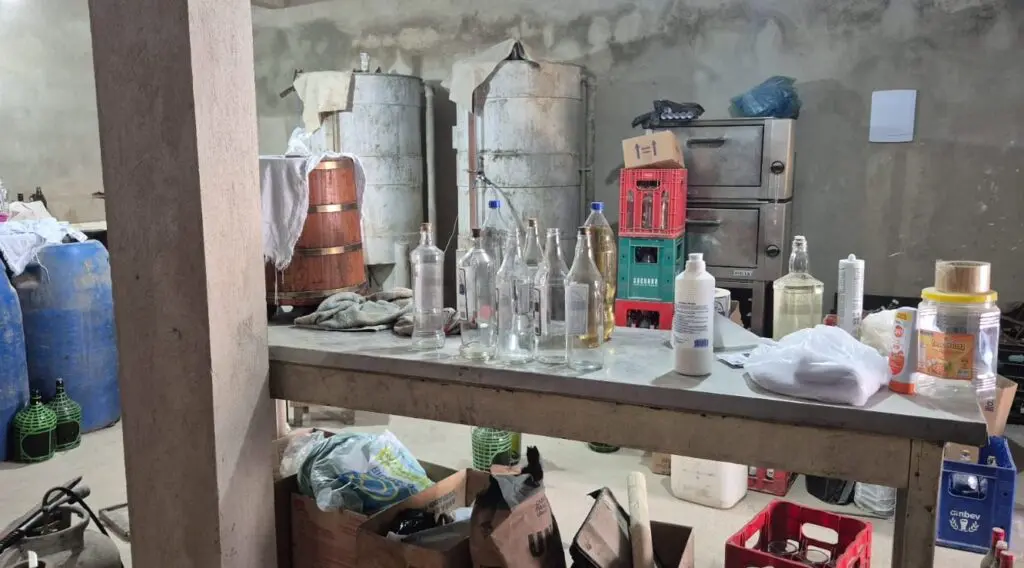 Imagem de uma fábrica clandestina com toneis e outros materiais, em condições precárias.