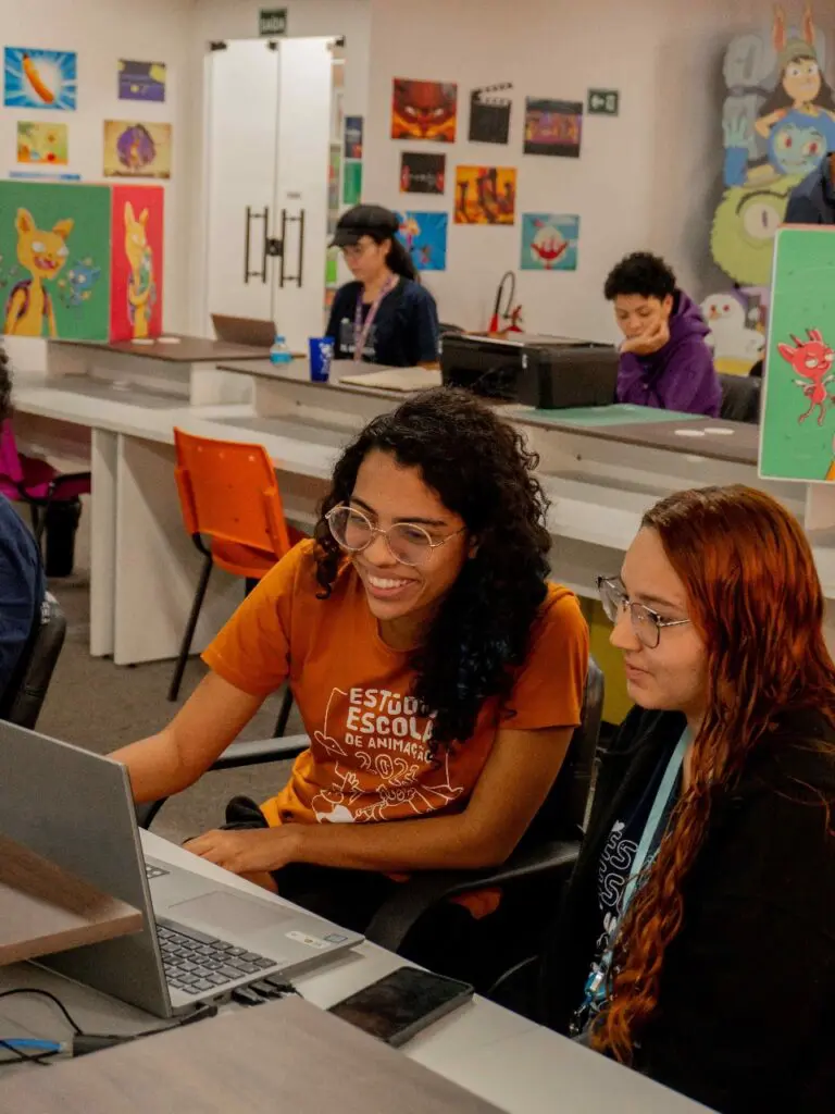 Uma sala de aula com 4 jovens sentado em frente a computadores durante uma aula de animação.