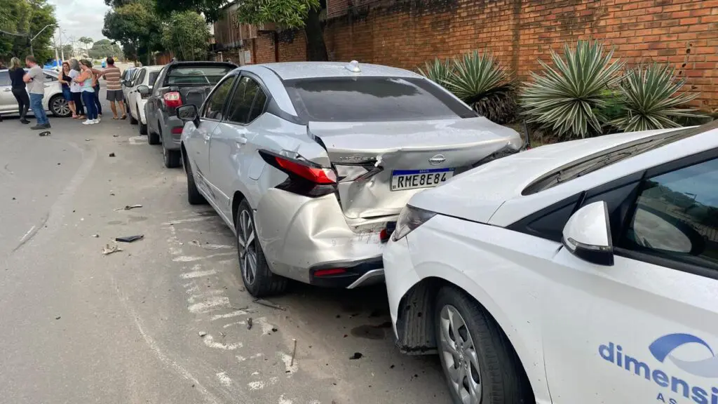 Imagem de uma rua com uma fileira de carros estacionados 3 deles danificados após um acidente.