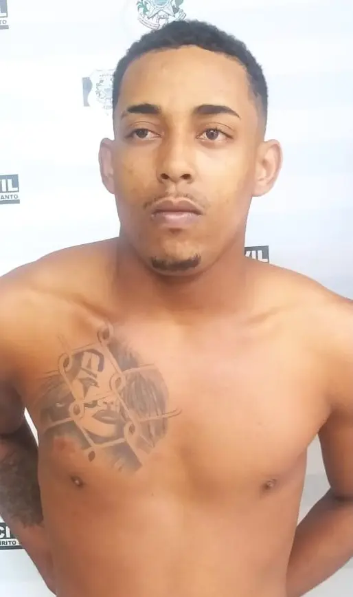 Imagem de um homem com os braços para traz, em frente a um banner da Polícia Civil.