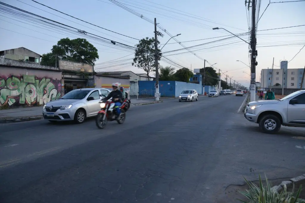 Imagem de uma rua com veículos trafegando pelo local, em destaque um carro ao lado de uma moto.