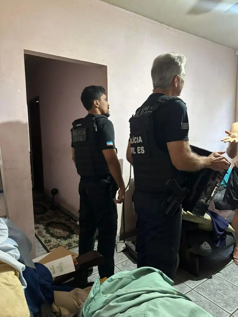 Dois policiais civis segurando um gabinete, durante as buscas na casa de uma mulher suspeita de fazer ameaças uma empresa dos Estados Unidos