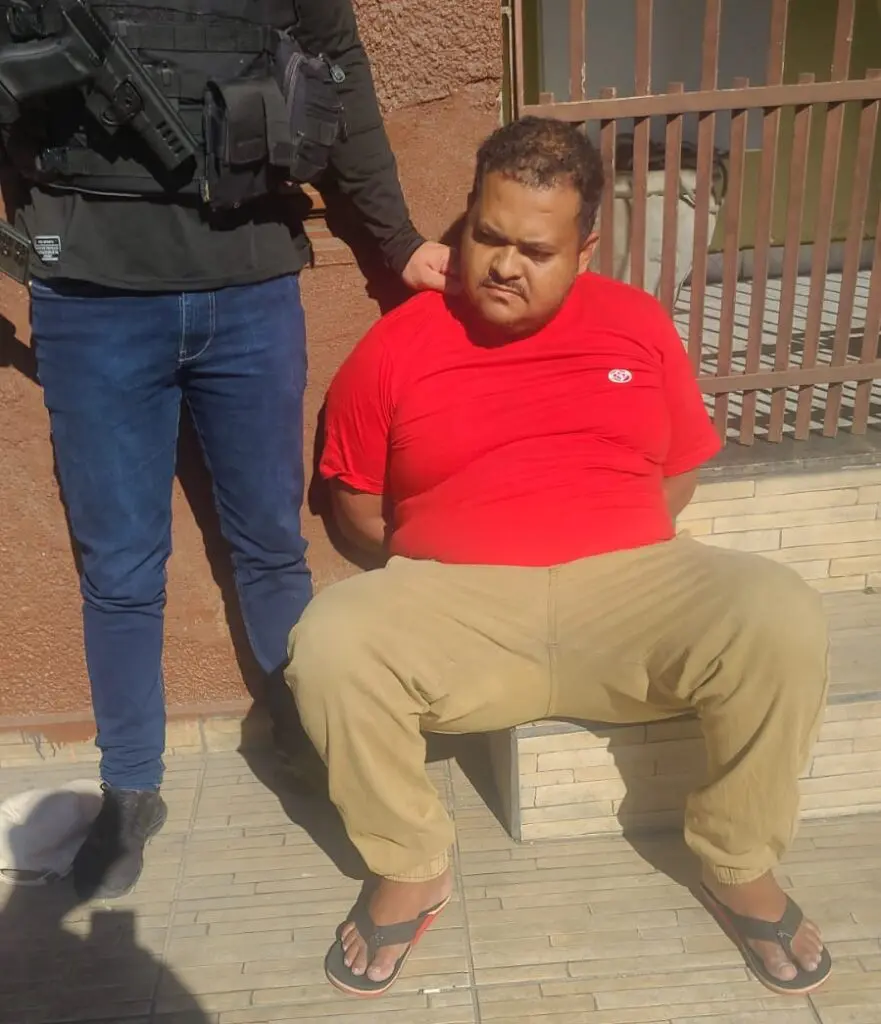 Imagem de um homem (Luiz Paulo Pereira da Silva, de 30 anos), sentado com as mãos para trás, ao lado de um policial civil, o sujeito detido ´é apontado como líder de uma quadrilha que furta e desmonta motocicletas para vender as peças no mercado paralelo.