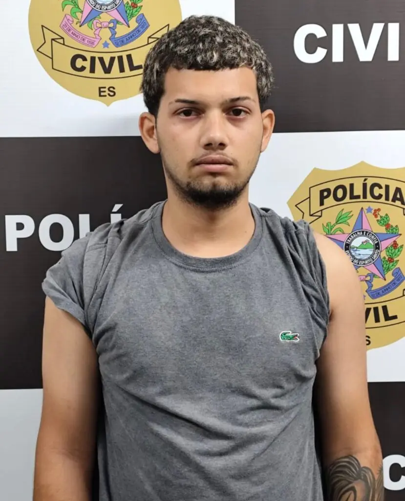 Imagem de um homem parado em frente a um banner da Polícia Civil.