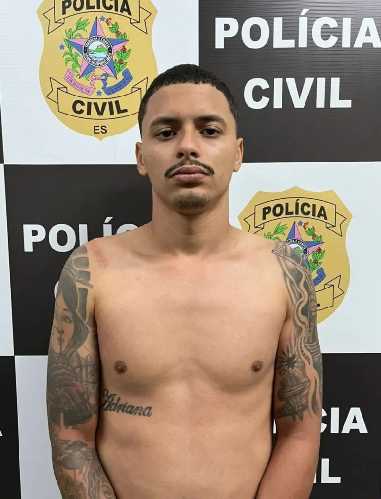 Imagem de um homem com os braços para frente parado em frente a um banner da Polícia Civil.