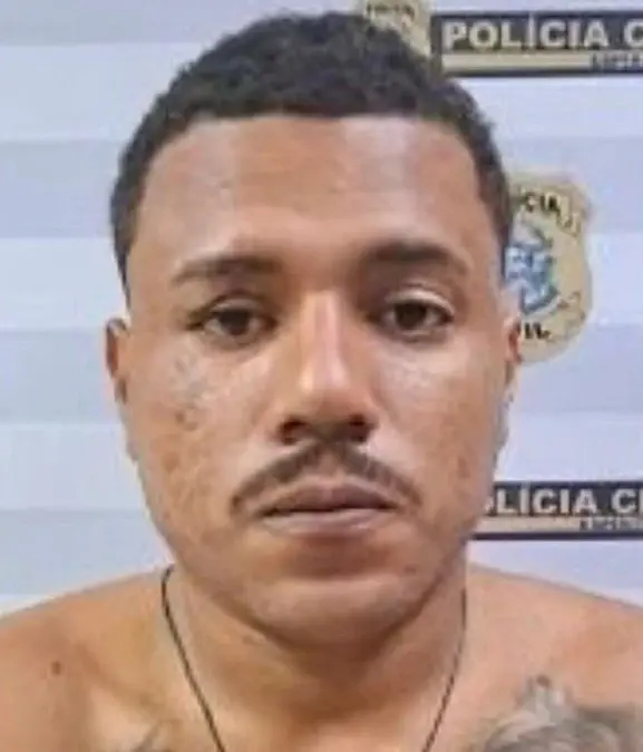 Imagem de um homem em frente a uma parede com o Banner da Polícia Civil, utilizado para fotografia de pessoas presas, (Sávio Soares de Souza), condenado a mais de 110 anos. 